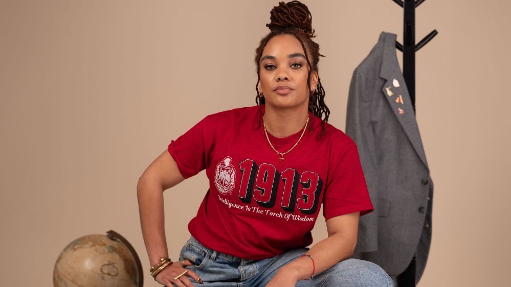 A woman sits on a metal stool wearing a red graphic T-shirt with '1913'